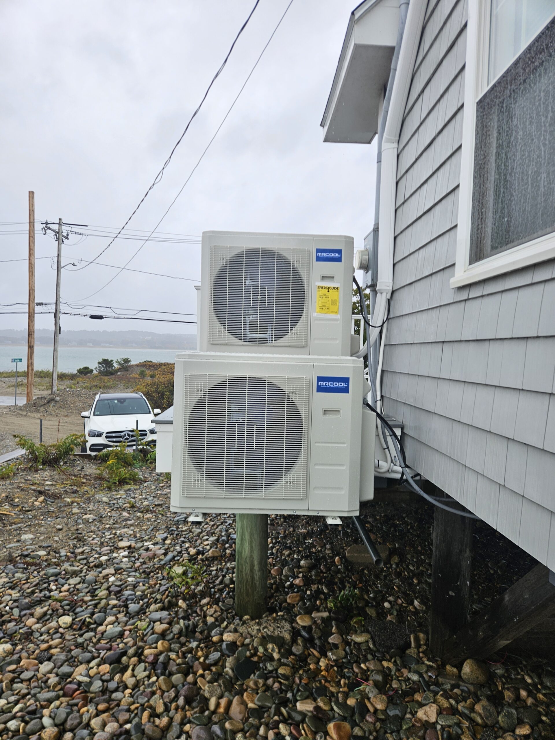 Two heat pump condensers installed along the side of a Massachusetts home